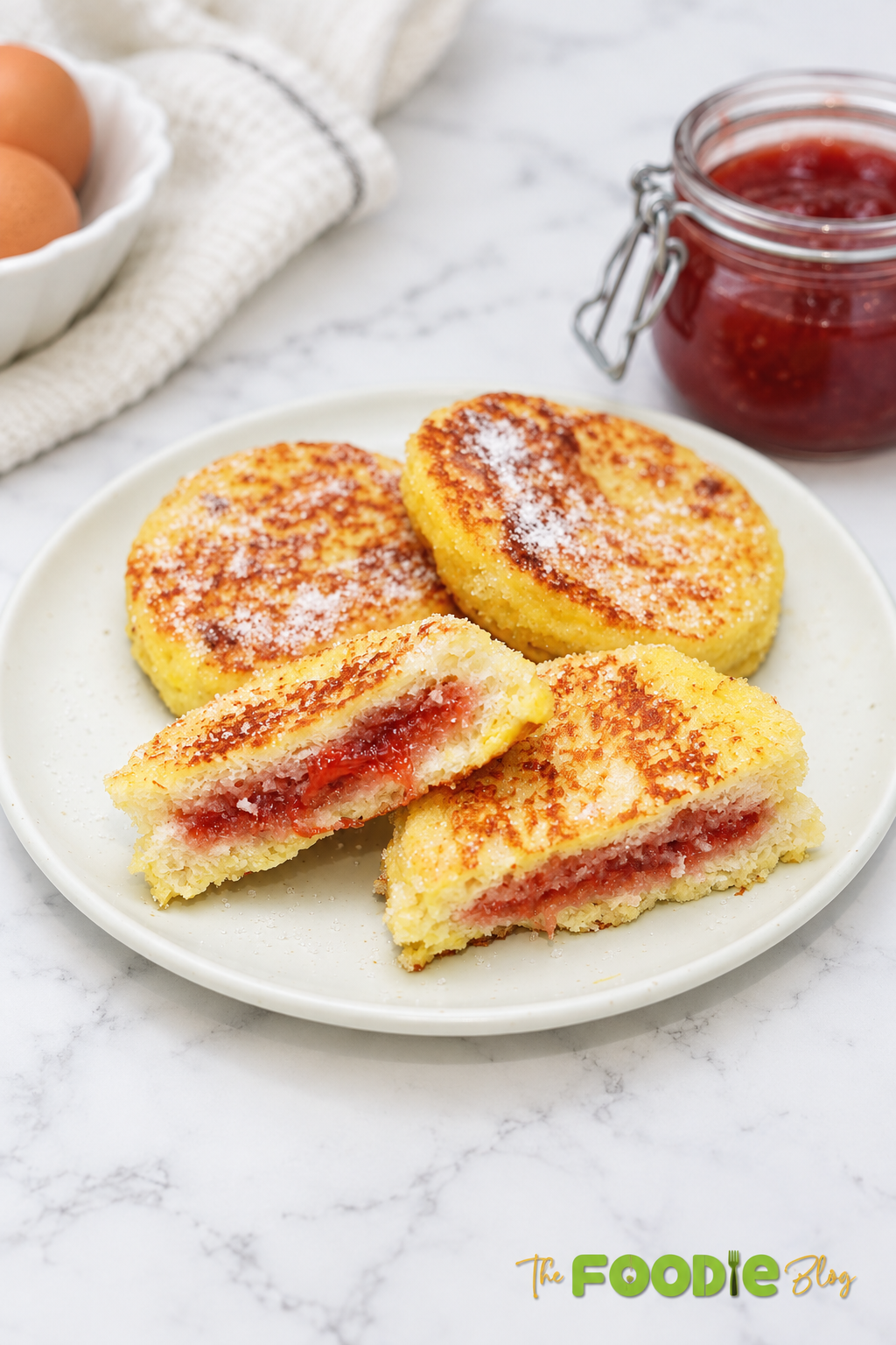 Strawberry jam stuffed French toast rounds served on a plate with sugar and strawberry jam.