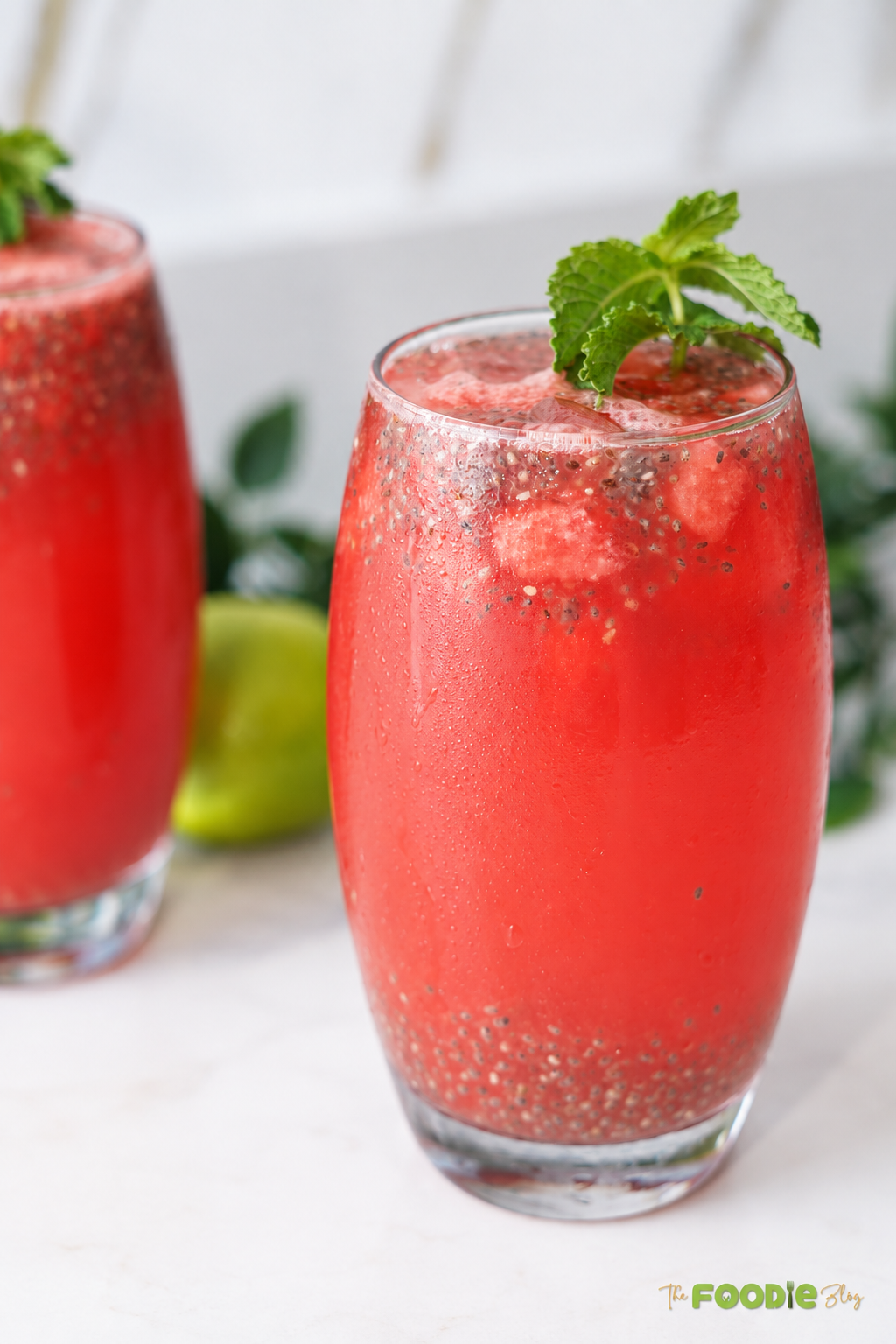 Close-up of chilled watermelon lemonade with basil seeds, watermelon pieces, ice, and mint.