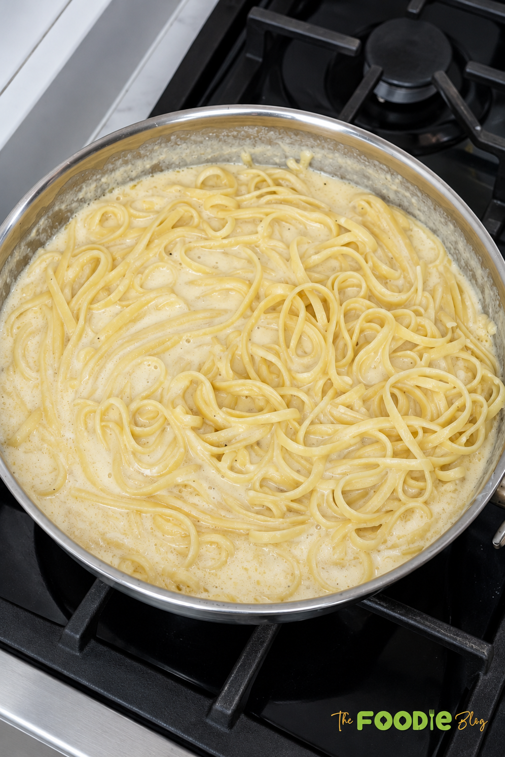 Fettuccine pasta simmering in creamy Alfredo sauce in a skillet on the stovetop.