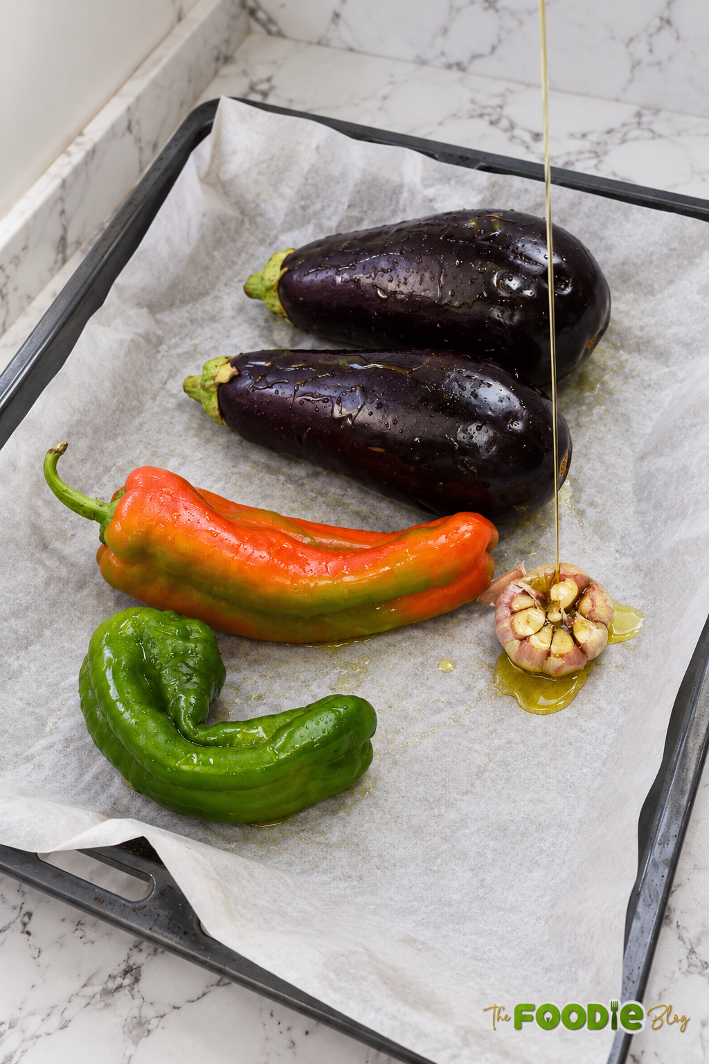 Eggplants, bell peppers, and garlic on a baking sheet being drizzled with oil before roasting.