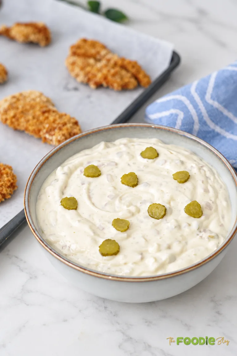 Homemade tartar sauce in a bowl topped with sliced dill pickles and served beside crispy fish