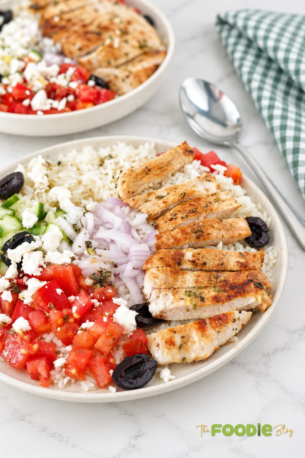 Greek chicken rice bowls served with grilled chicken, rice, tomatoes, cucumber, feta, red onion, and black olives.