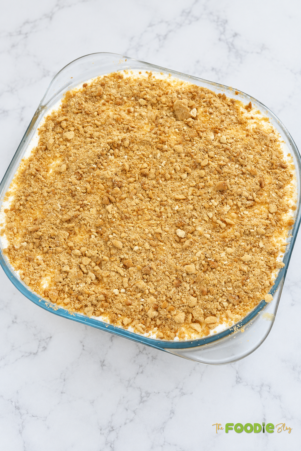 Whole no-bake peach dessert in a glass baking dish topped with crushed digestive biscuits.