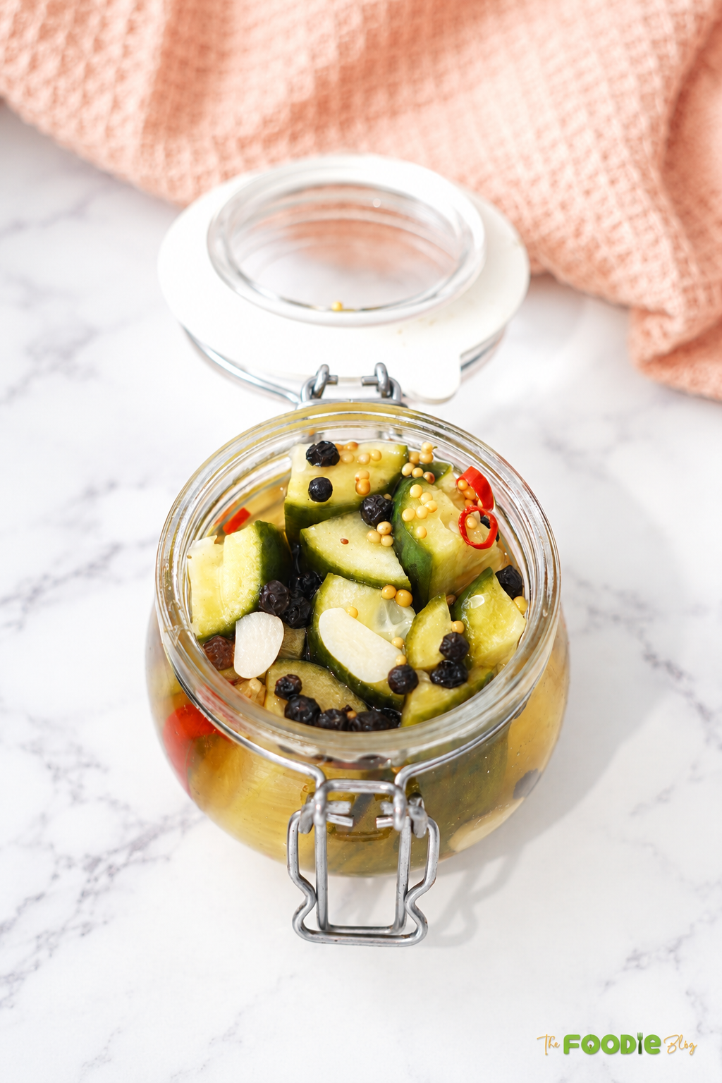 Close-up of homemade refrigerator dill pickles in a glass jar with garlic, mustard seeds, peppercorns, and chili.