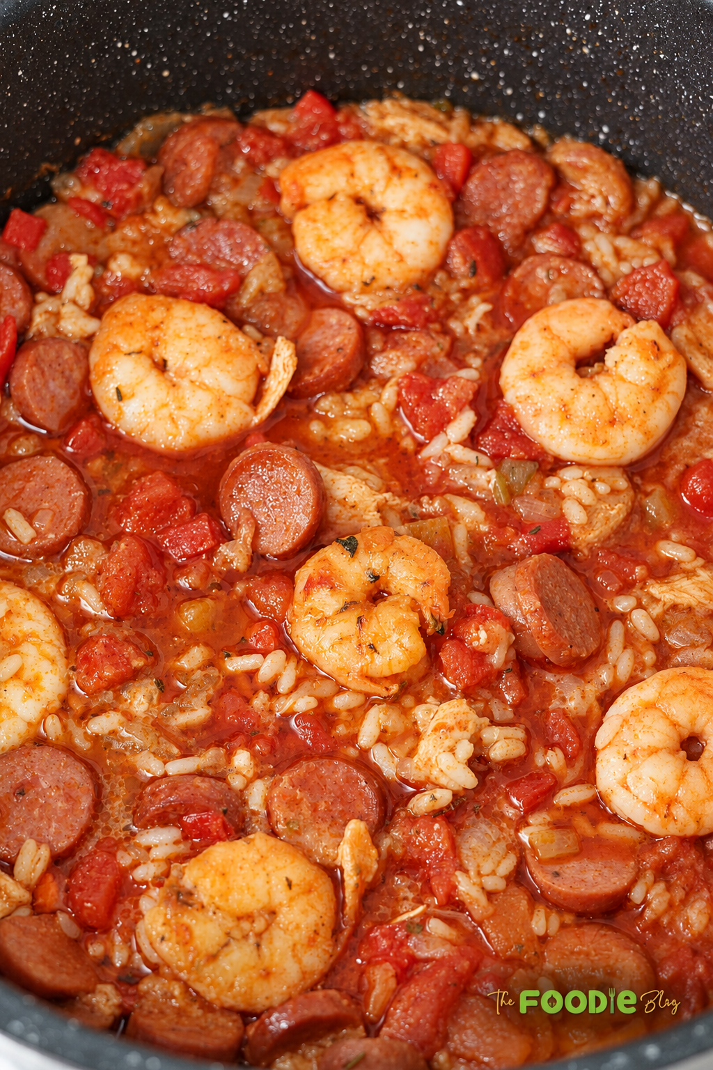 Chicken shrimp and sausage jambalaya cooking in a pot with rice, tomatoes, and Cajun spices.