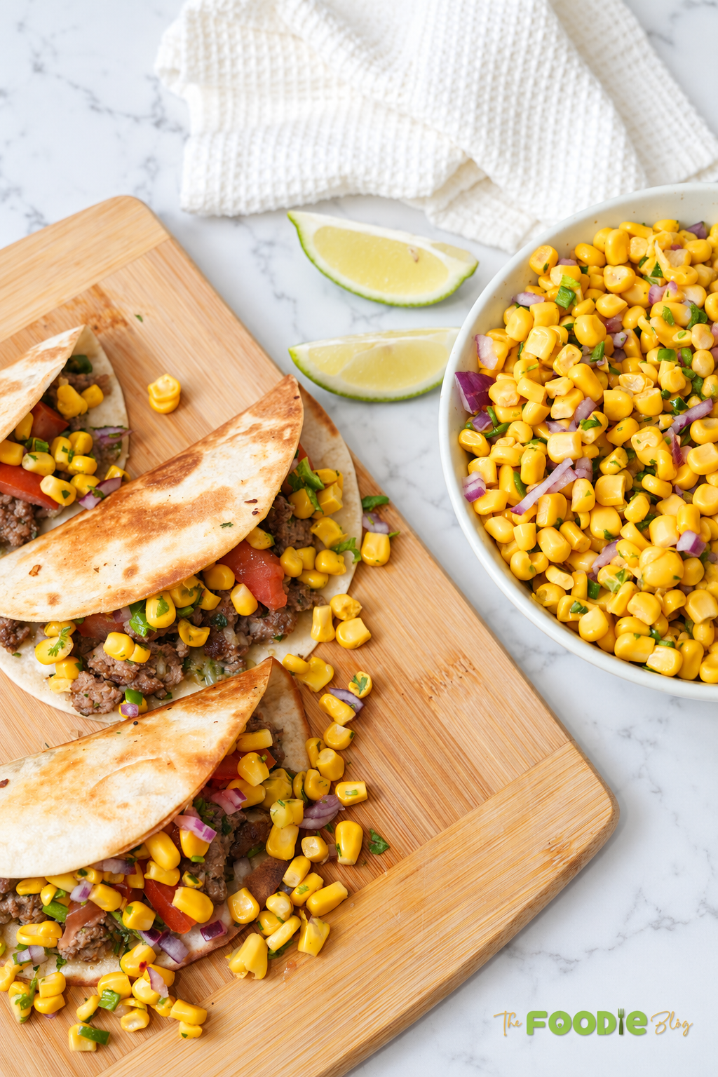 Fresh corn salsa served with beef tacos and lime wedges on a wooden board.
