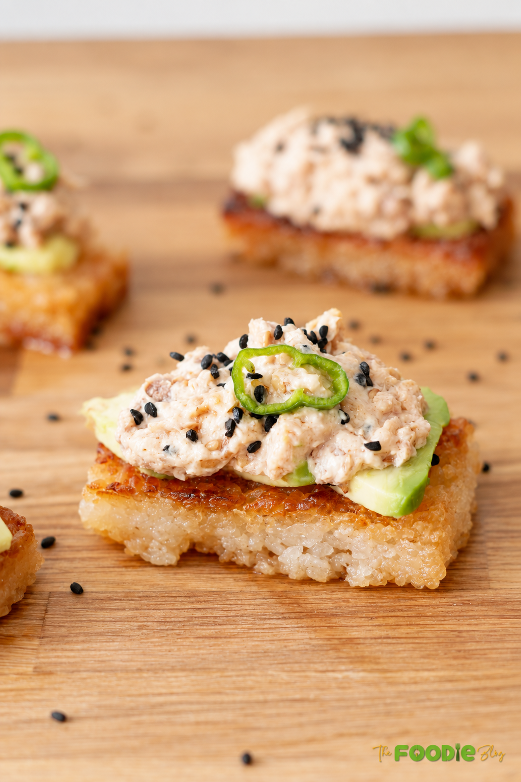Close-up of crispy sushi rice topped with avocado, creamy spicy tuna, jalapeño, and black sesame seeds.