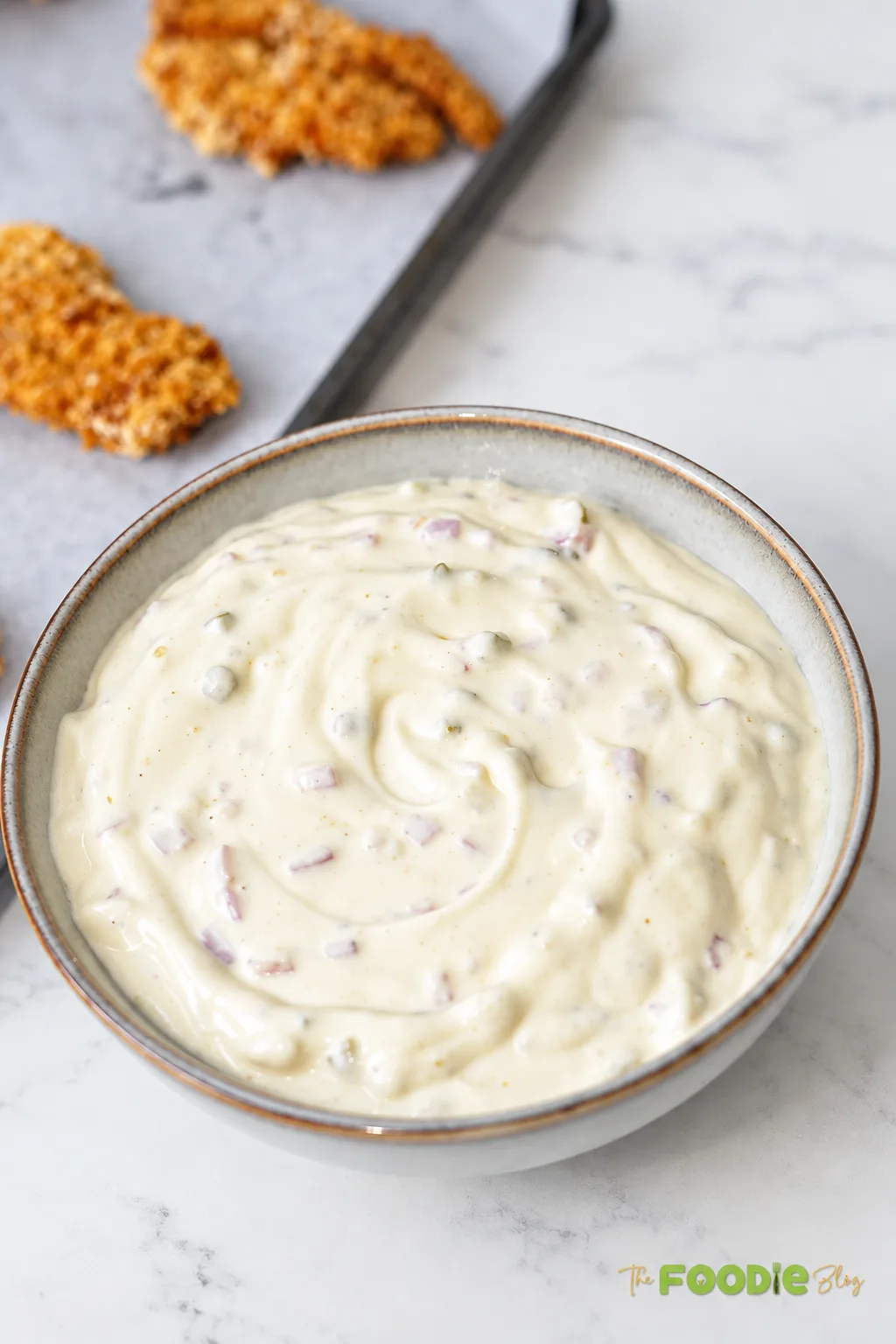 Creamy tartar sauce with finely chopped onion and dill pickles in a serving bowl