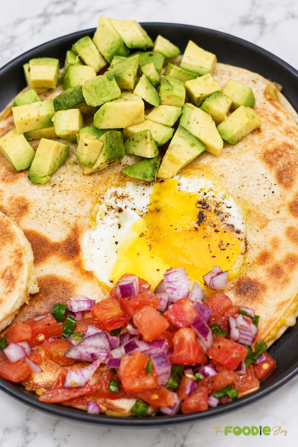 Egg quesadilla with a runny fried egg in the center, avocado, tomato salsa, red onion, and jalapeño.