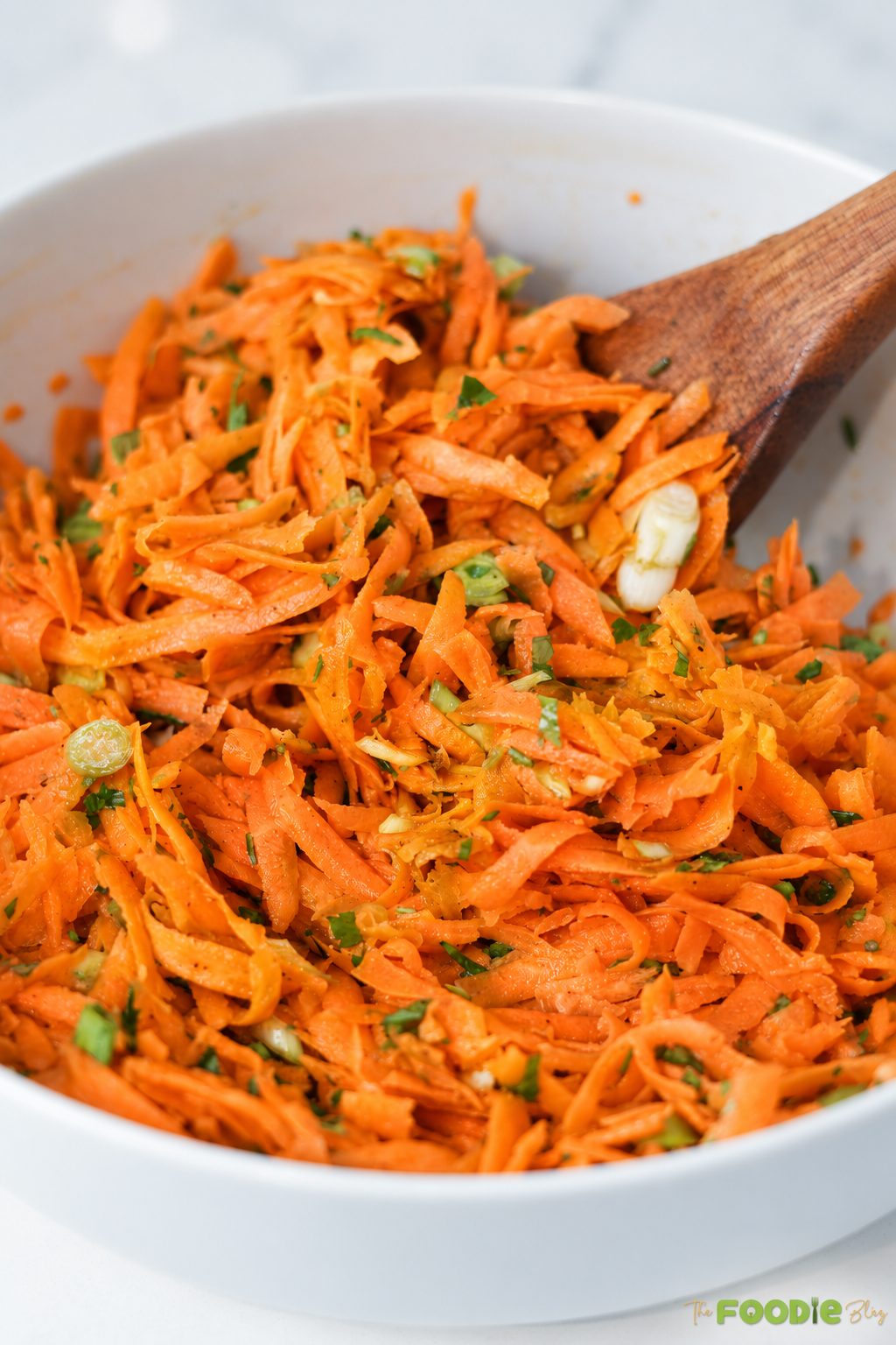 Close-up of grated carrot salad with parsley and sliced green onions.