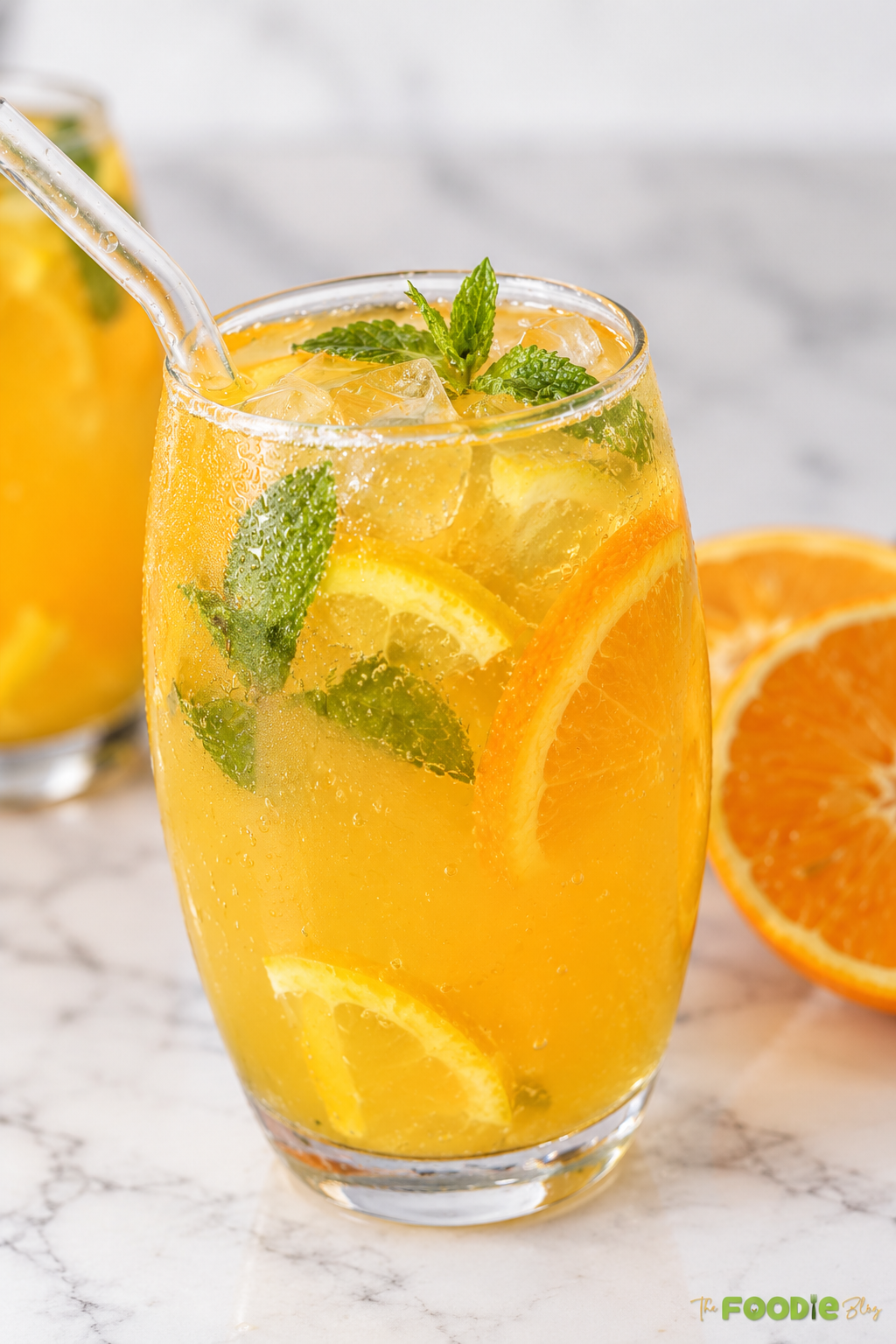 Close-up of orange mojito with ice cubes, mint leaves, orange slices, and a glass straw.