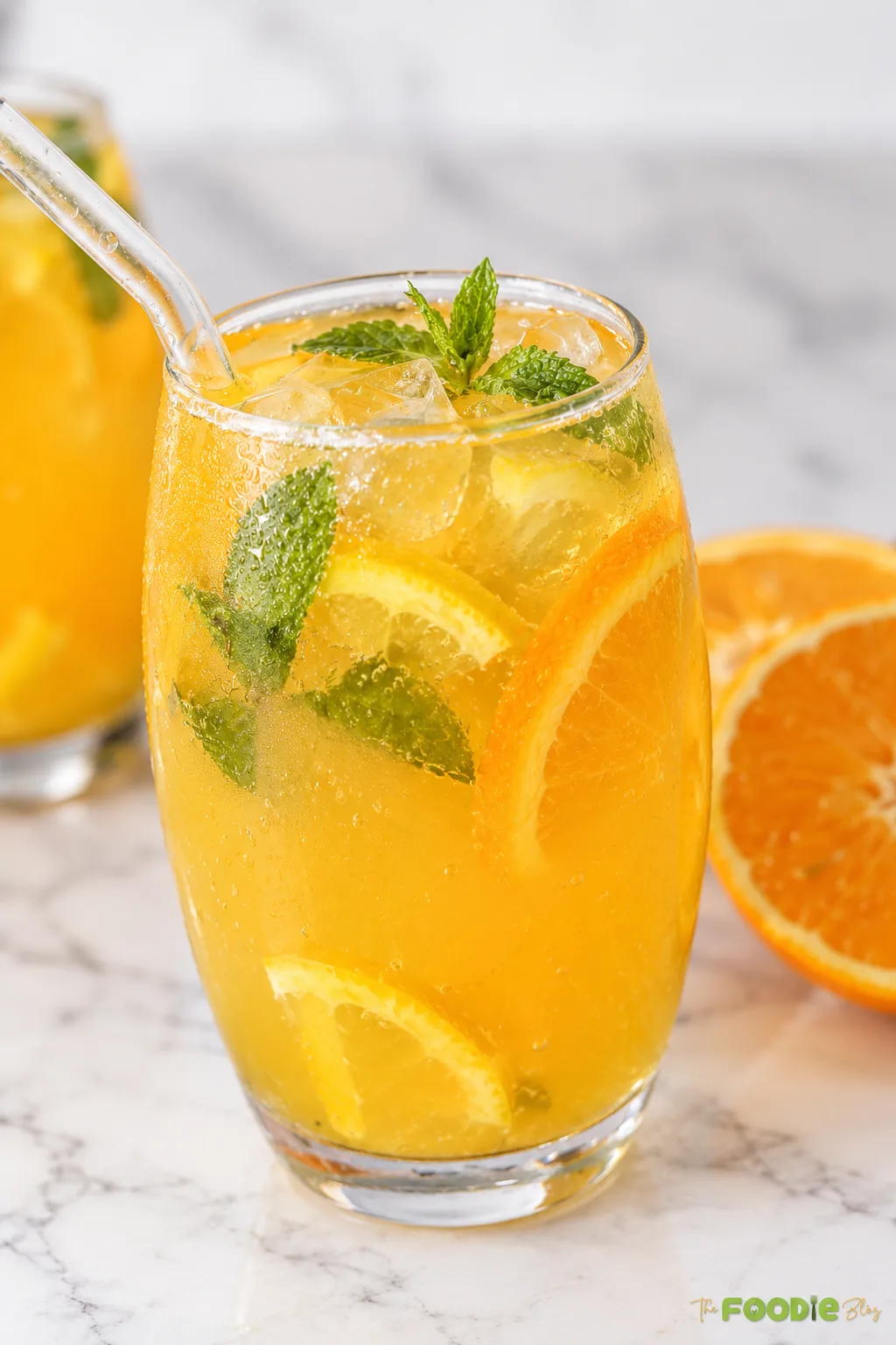 Close-up of orange mojito with ice cubes, mint leaves, orange slices, and a glass straw.