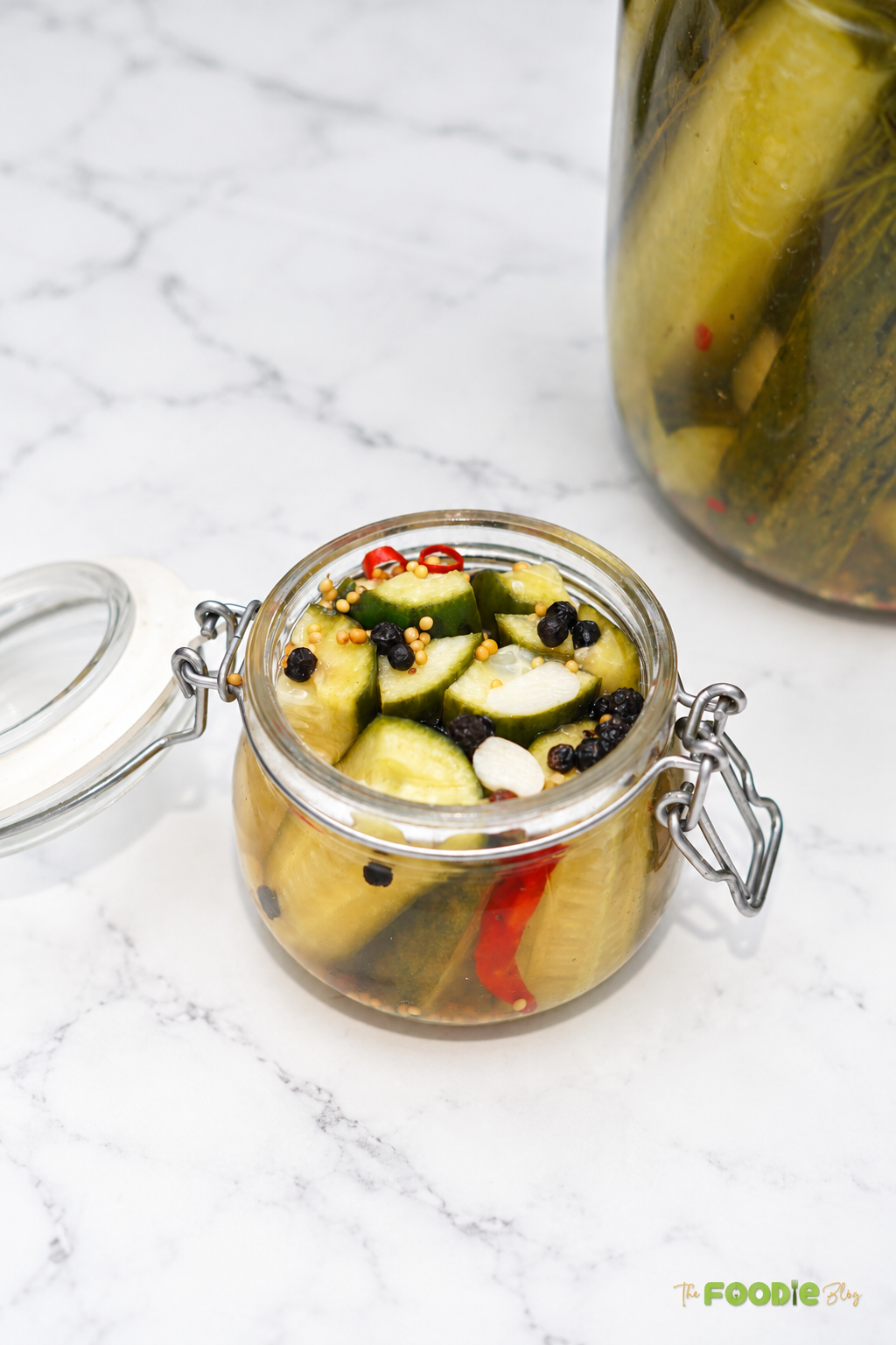 Small glass jar filled with sliced refrigerator dill pickles, garlic, mustard seeds, peppercorns, and red chili.