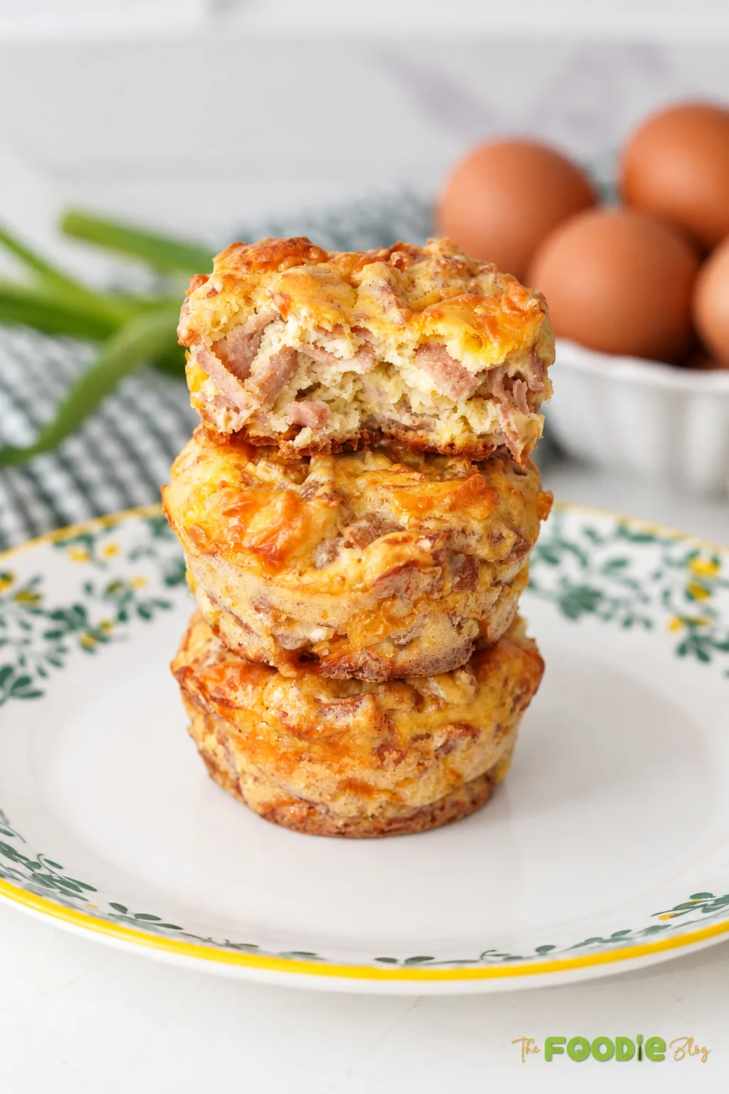 Three golden sausage egg and cheese breakfast muffins stacked on a serving plate.