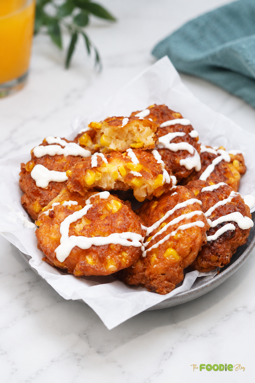 Golden sweet corn fritters with feta arranged on a serving platter and drizzled with creamy sauce.