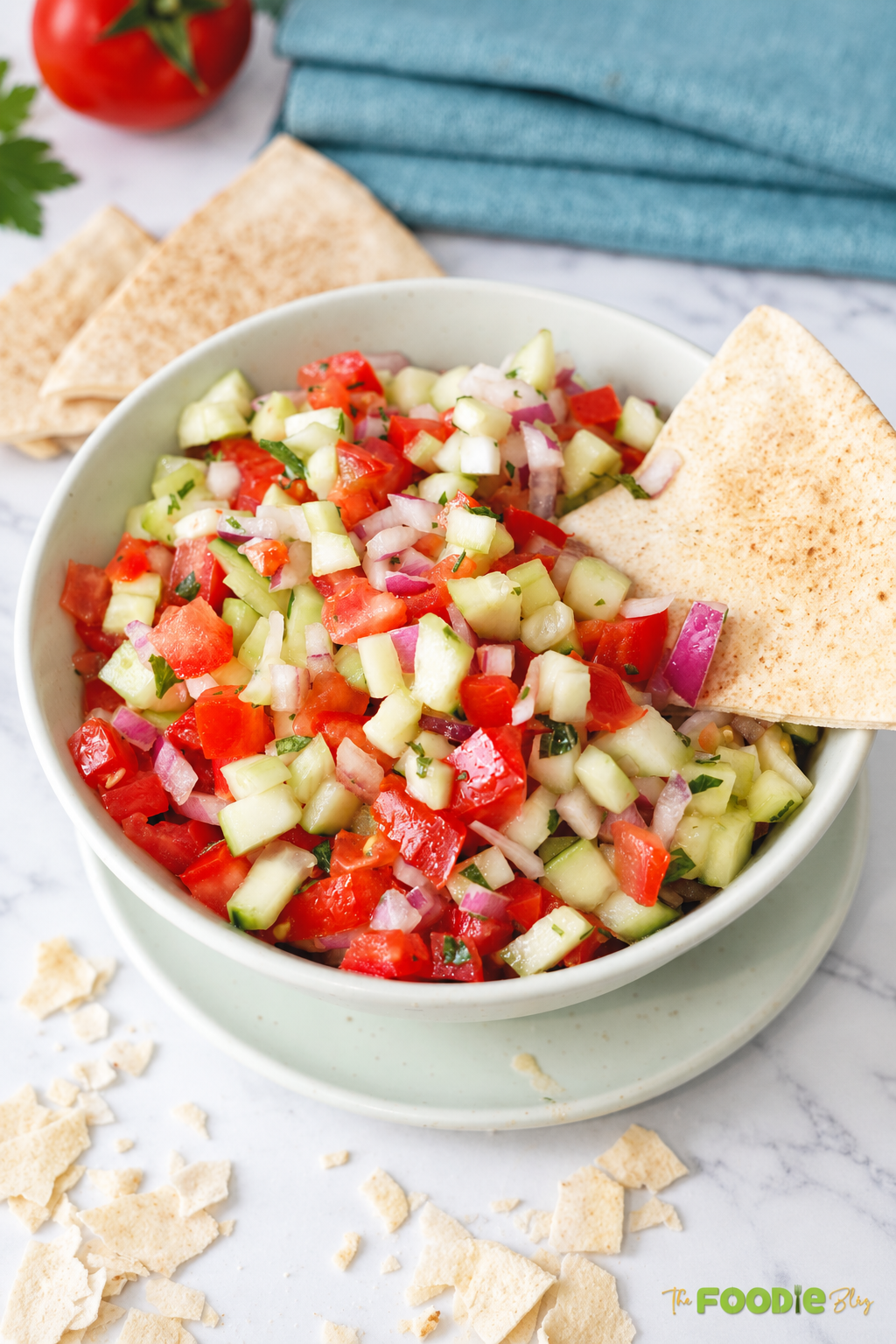 Close-up of fresh tomato cucumber salad with red onion, parsley, and mint in a serving bowl with pita bread.