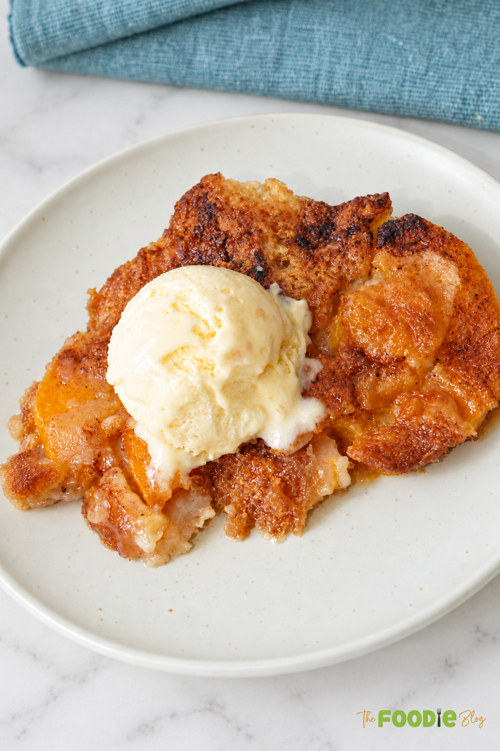 Close-up of canned peach cobbler on a plate topped with melting vanilla ice cream.