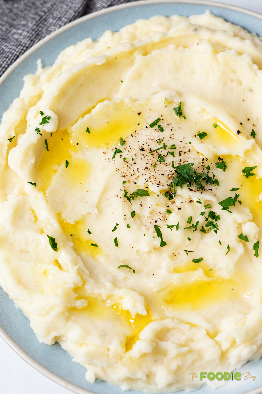 Close-up of creamy mashed potatoes with melted butter, parsley, and black pepper.