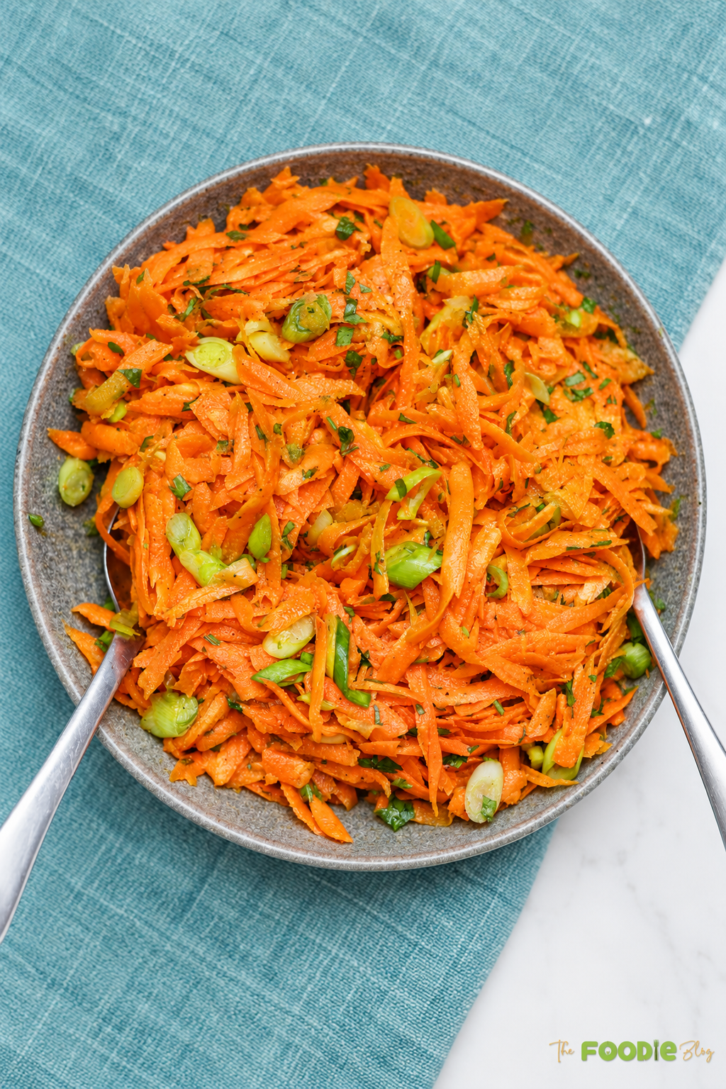 Grated carrot salad served in a bowl with green onions and parsley.