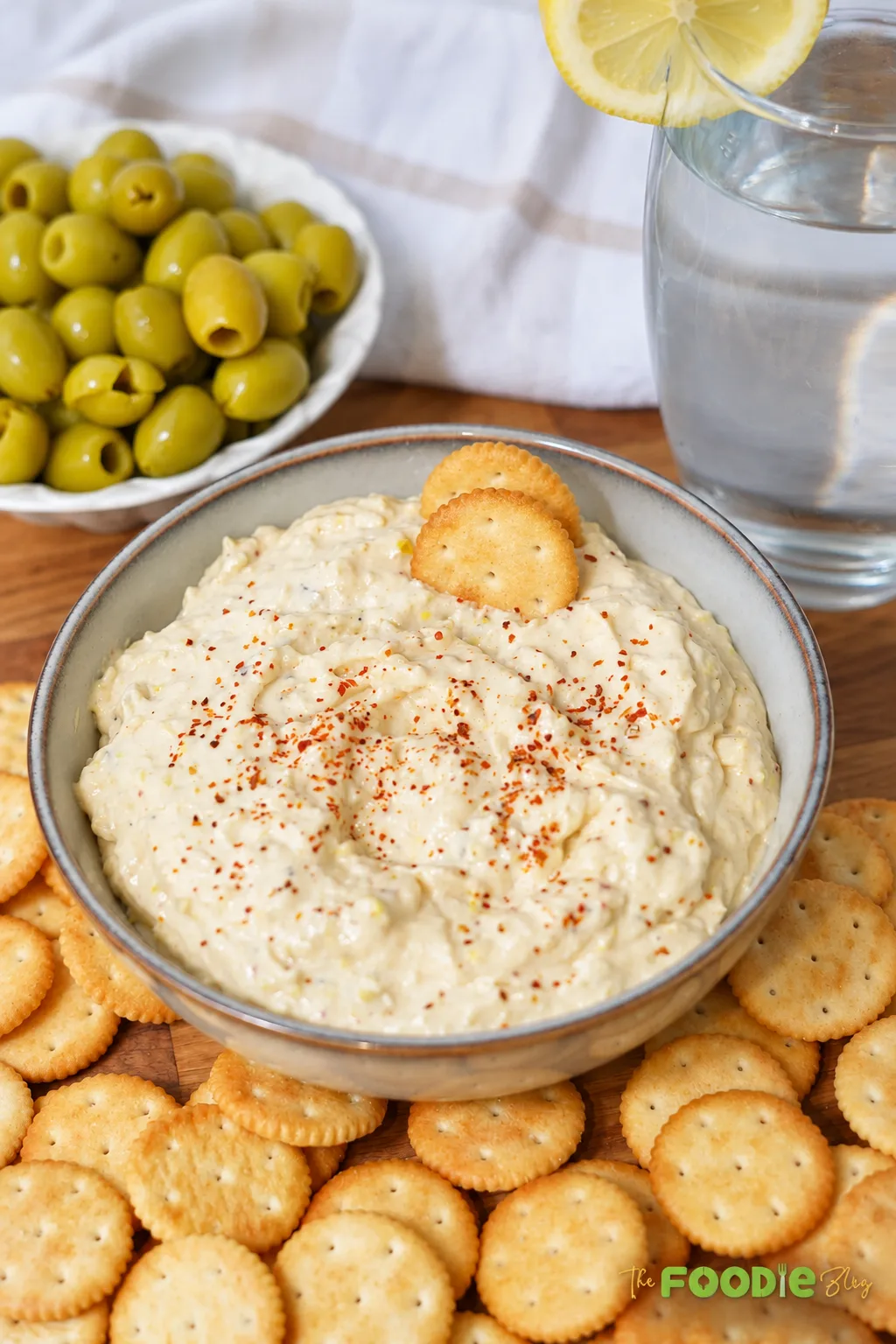 Close-up of creamy green olive dip topped with paprika and served with crackers.