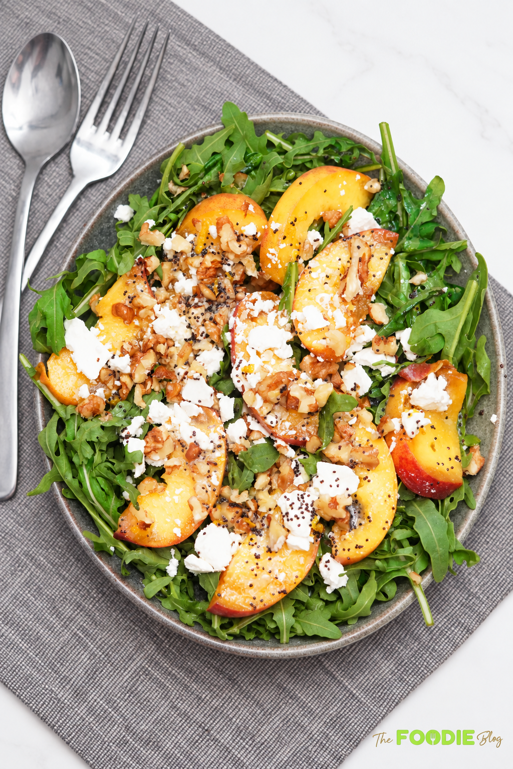 Close-up of peach arugula salad with sliced peaches, feta cheese, walnuts, and poppy seed dressing.