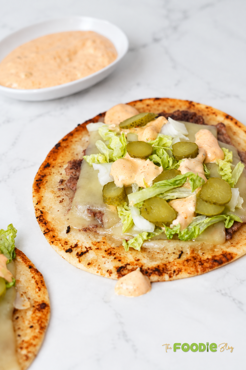 Close-up of a smash burger taco filled with beef, melted cheese, lettuce, pickles, onions, and creamy burger sauce.