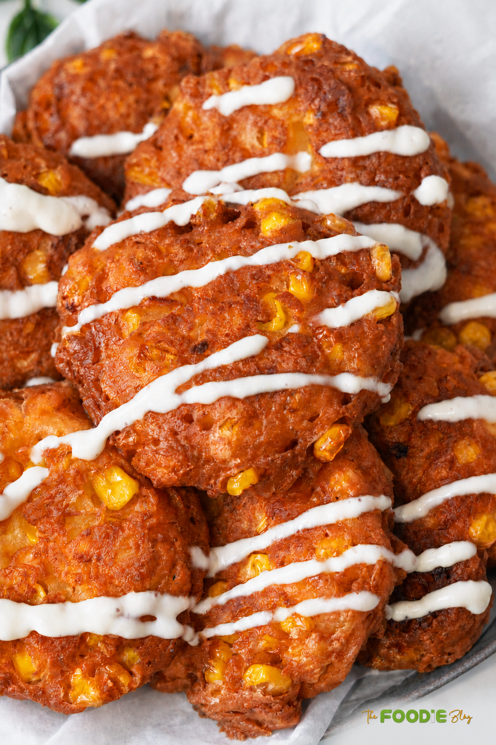 Close-up of golden crispy corn fritters with visible sweet corn kernels and a creamy sauce drizzle.