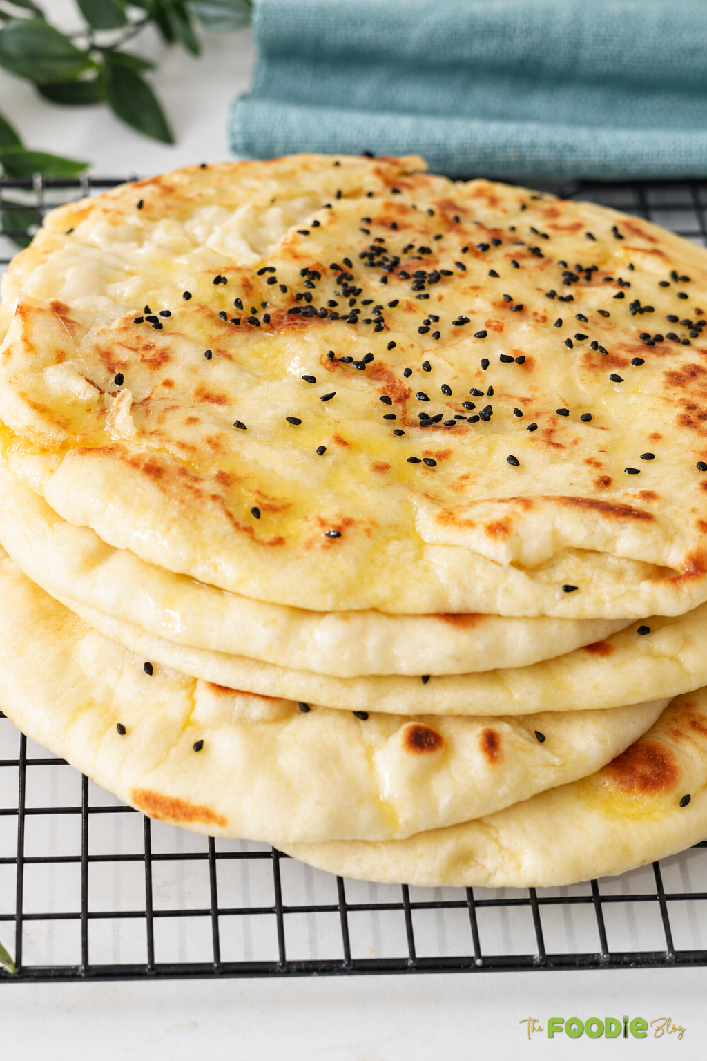 Stack of soft cheese naan breads topped with melted butter and black sesame seeds.