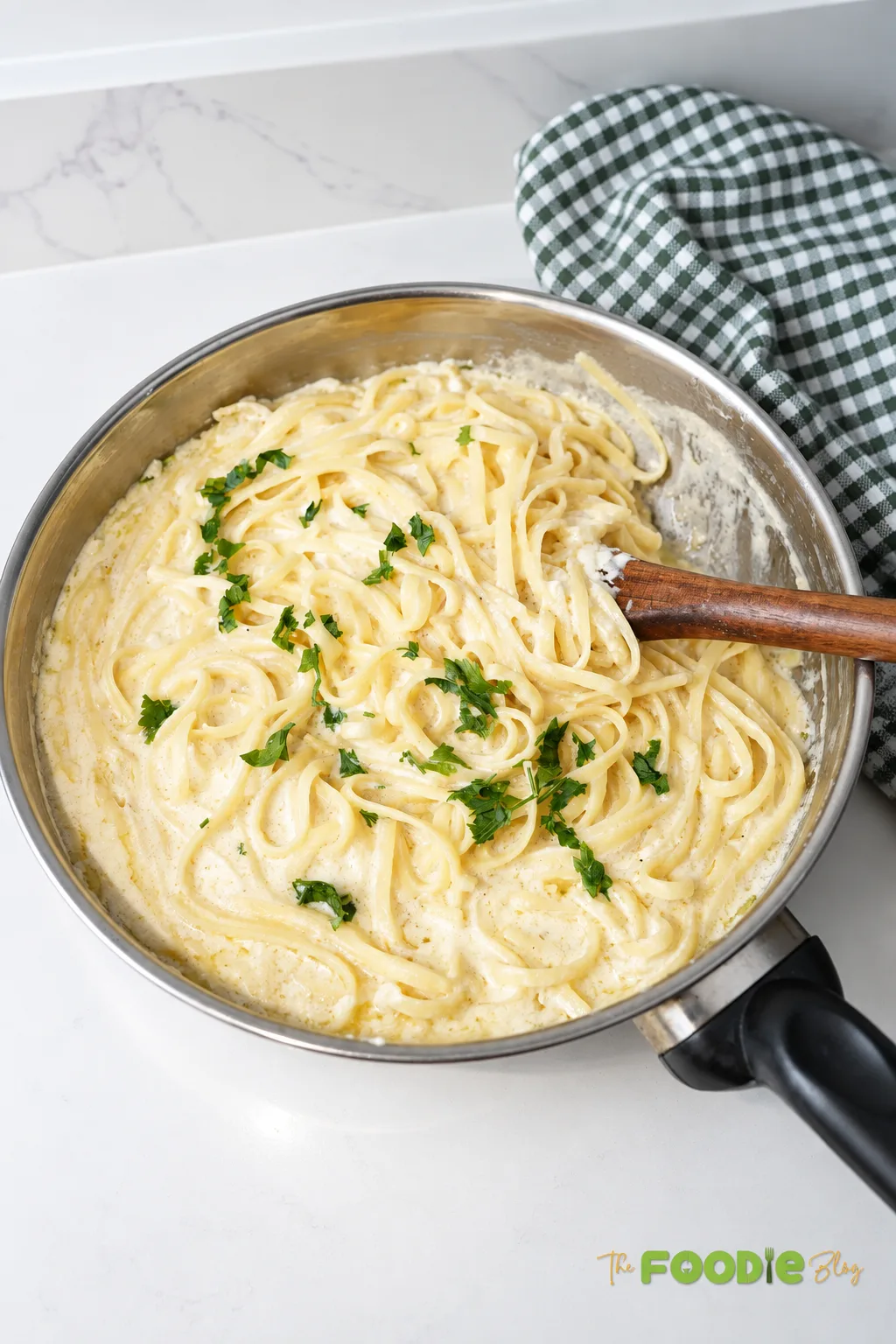 Creamy fettuccine Alfredo in a skillet with parsley and a wooden spoon ready for serving.