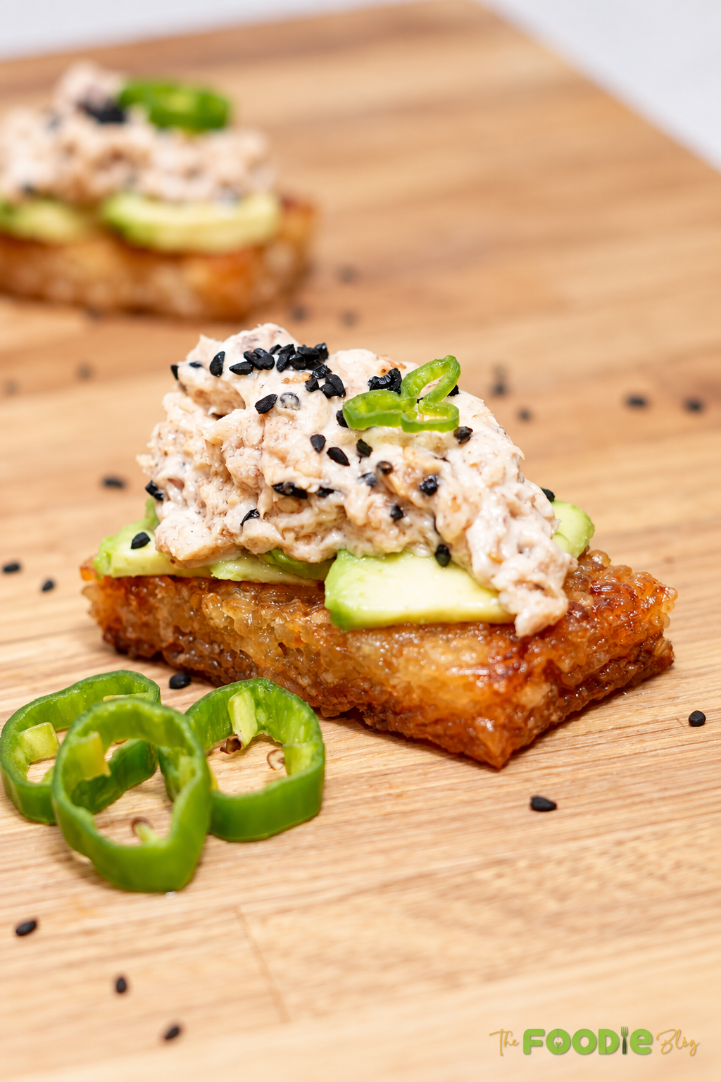 Close-up of crispy rice topped with avocado, creamy spicy tuna, sesame seeds, and green chili.