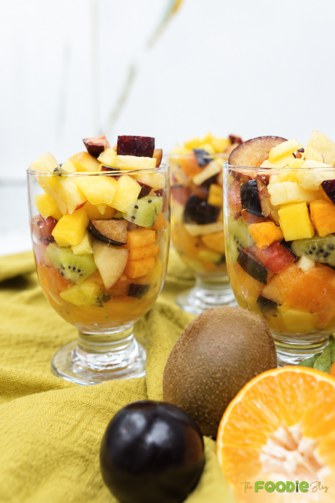 Close-up of fresh fruit salad in a glass with pineapple, mango, kiwi, plums, apples, and persimmons.
