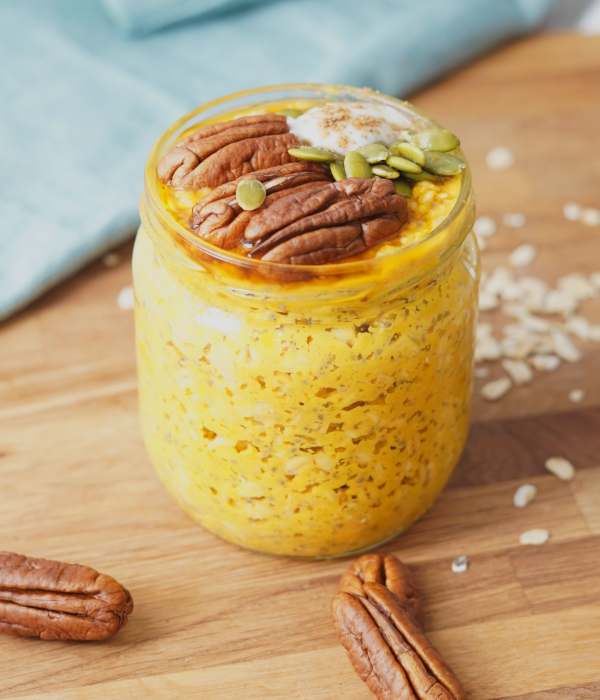 Close-up of a jar of pumpkin pie overnight oats with pecans, pumpkin seeds, and a creamy topping.